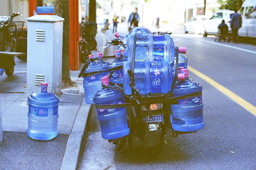 A delivery motorbike loaded with large blue 19-litre water jugs parked on a city street