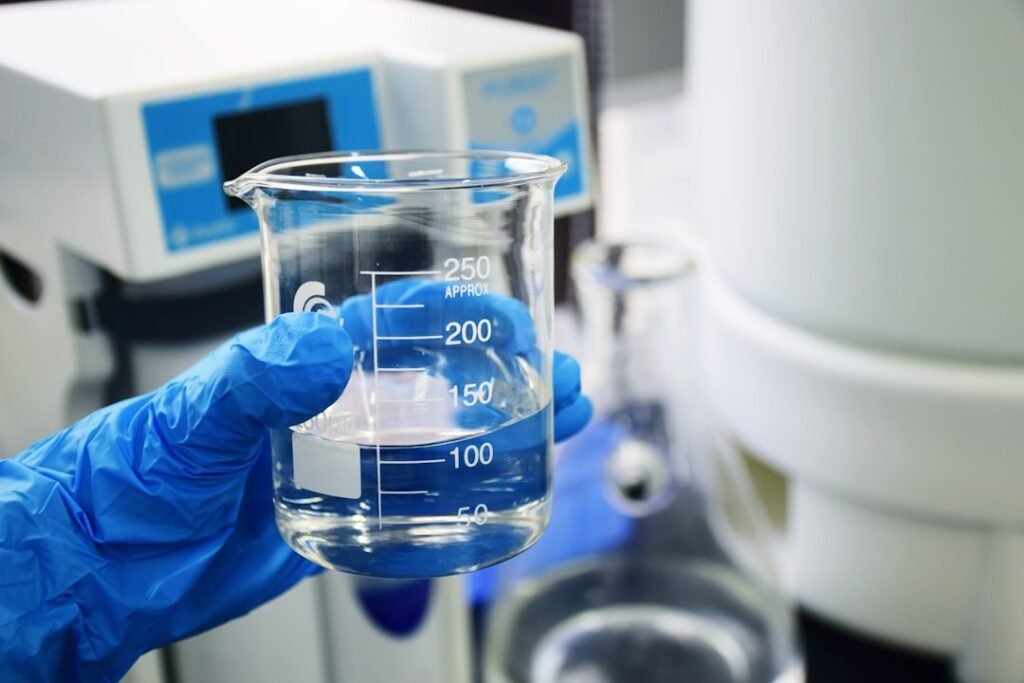Lab technician in blue gloves holding a water sample beaker for quality testing, representing TDS and pH compliance checks for mineral water