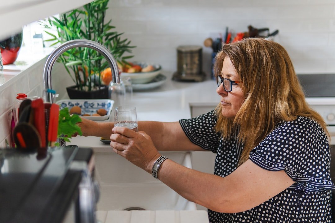 Woman filling a glass with water from a kitchen faucet, illustrating tap water safety concerns in Multan households