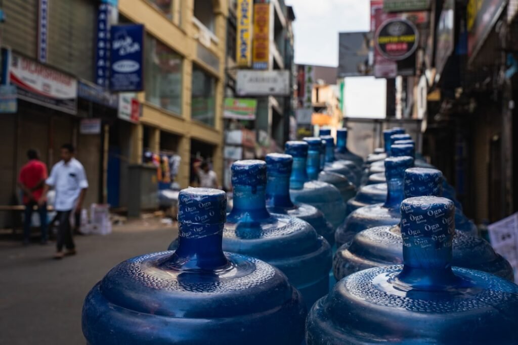 Rows of large 19-litre water jugs lined up on an urban street, ready for home and office delivery